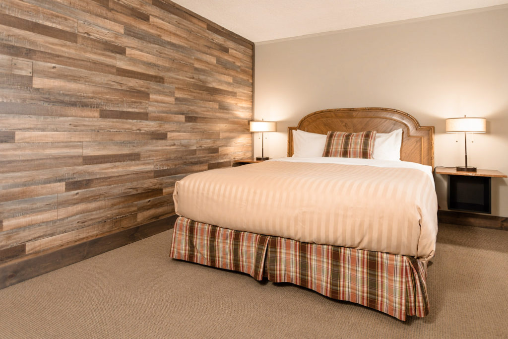 A standard king room with a wood pattern accent wall, bedside tables, lamps and 5 pillows